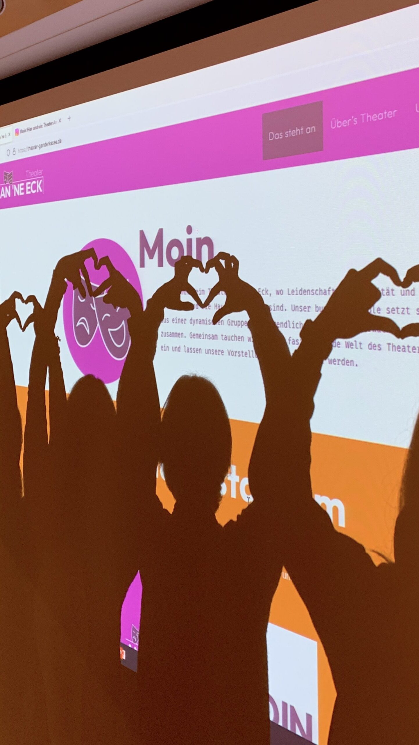 Das Ensemble steht vor einer Projektion der Website.