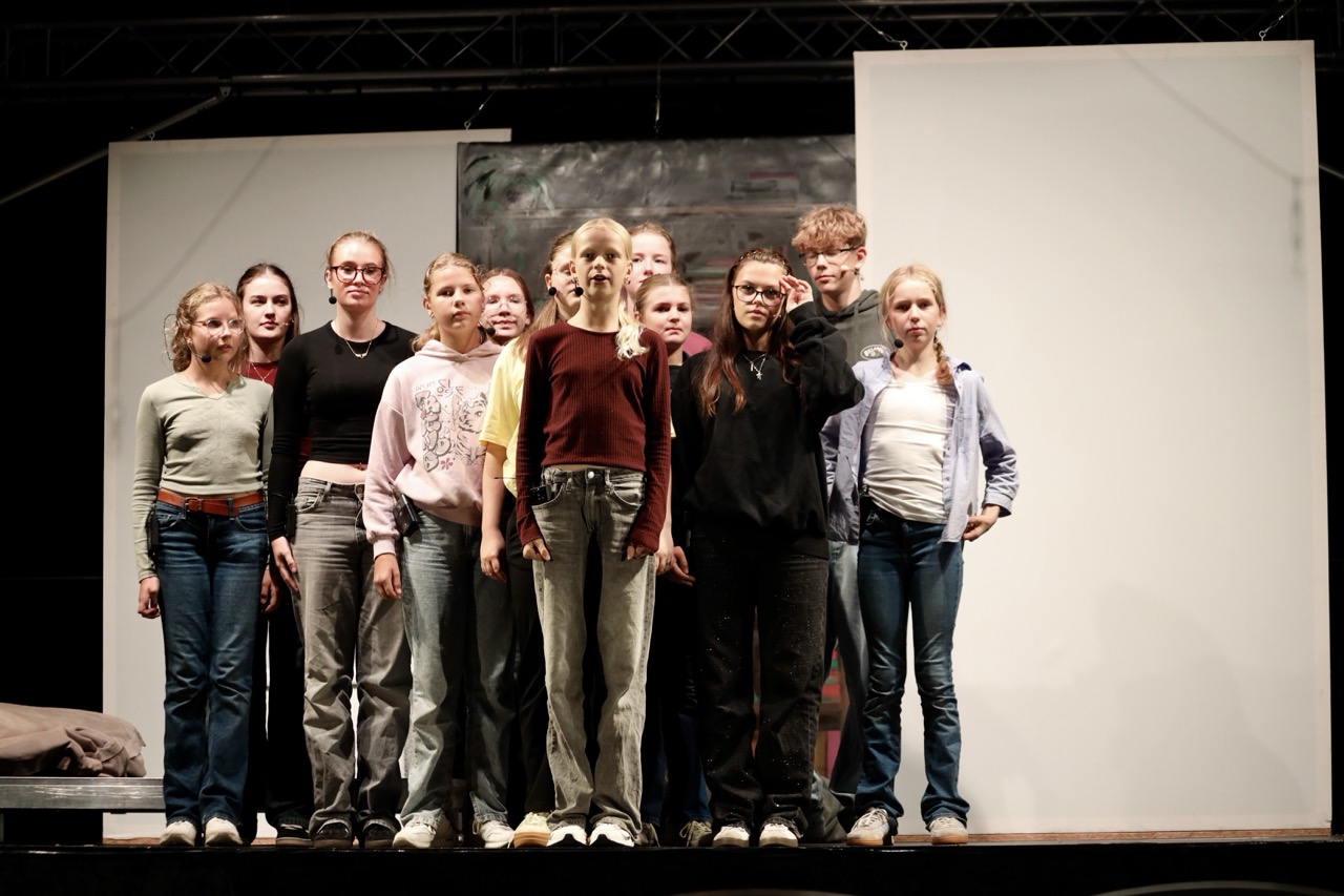 Eine Gruppe von Schauspielenden stehen im Pulk auf der Bühne.